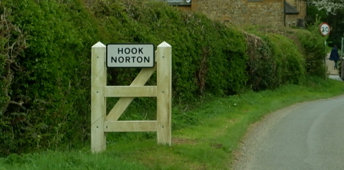 This image: a road sign for Hook Norton on a grassy verge.
							 The map: The map has zoomed into Hook Norton, with a dotted line
							 showing the site boundary for the proposals to the northwest of
							 the village. Several nearby facilities to the site are labelled
							 on the map.